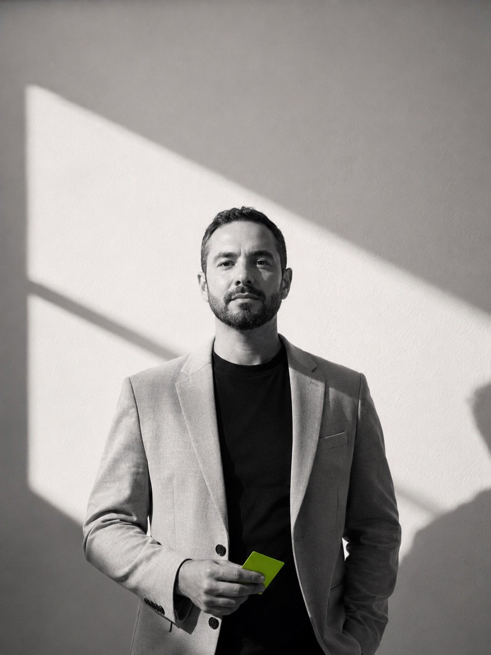 Retrato editorial em preto e branco de um profissional de blazer segurando um cartão verde