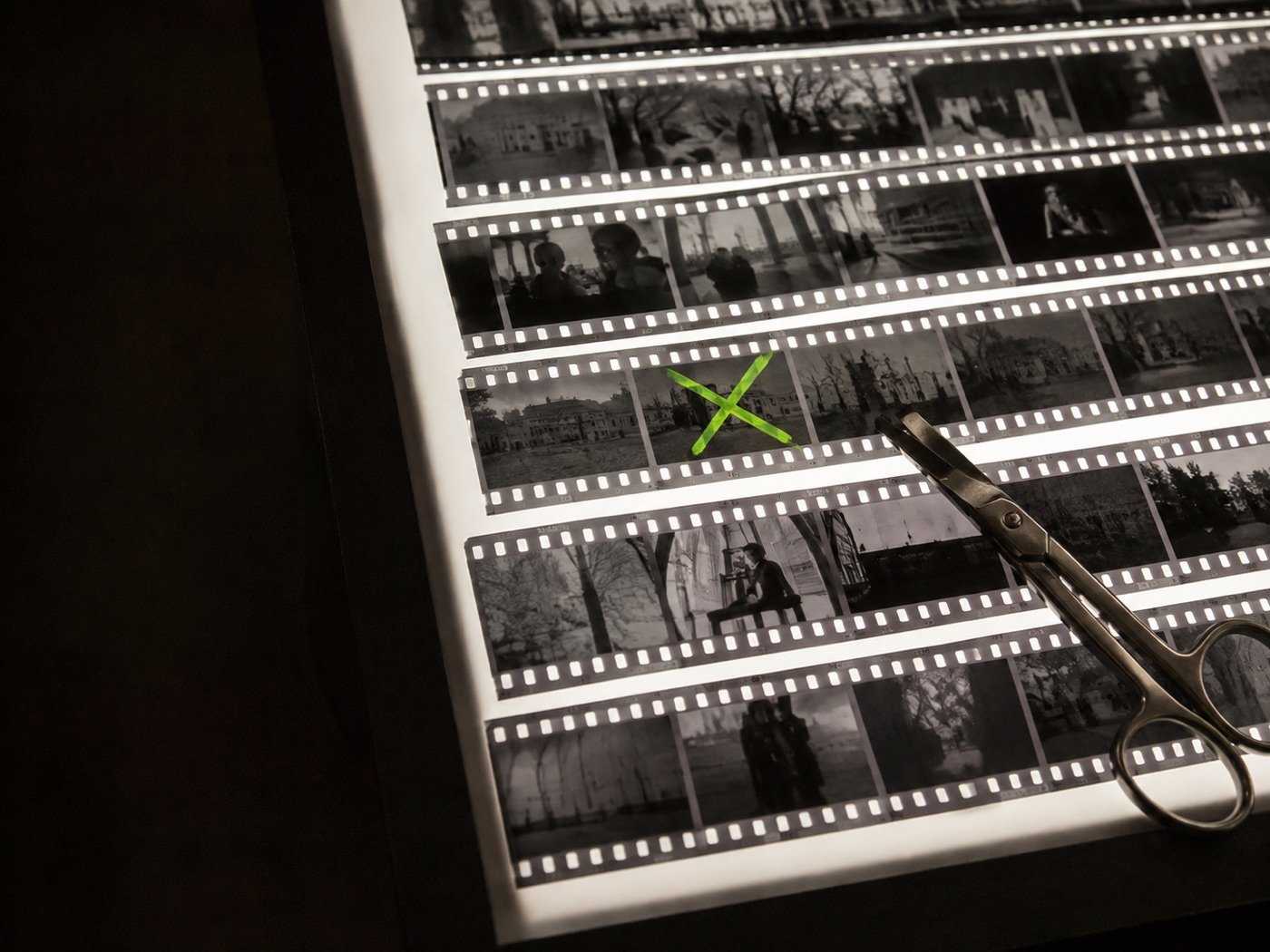 Tiras de negativo sobre mesa de luz com uma tesoura e um fotograma marcado com X verde