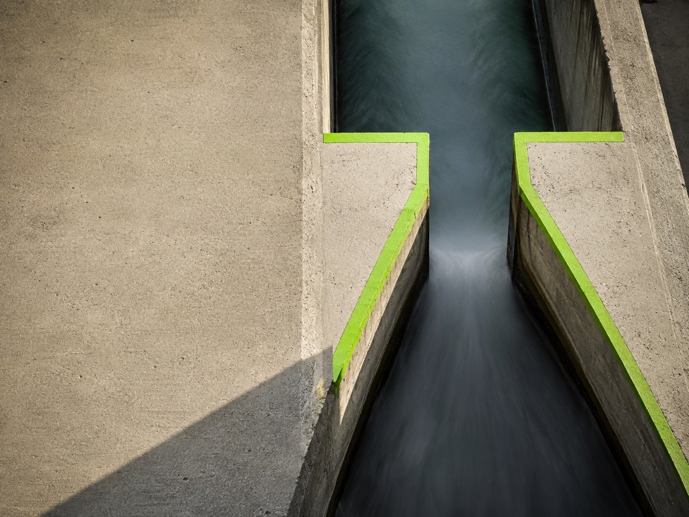 Canal de concreto em forma de funil com bordas verdes conduzindo a água para um único fluxo